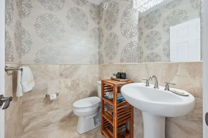 Powder room with damask wallpaper, marble wainscoting and pedestal sink