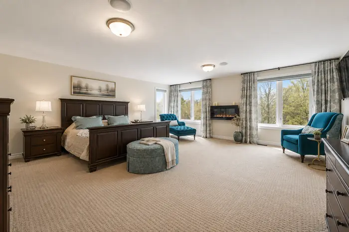 Expansive primary bedroom with wall fireplace and greenspace views, virtually staged