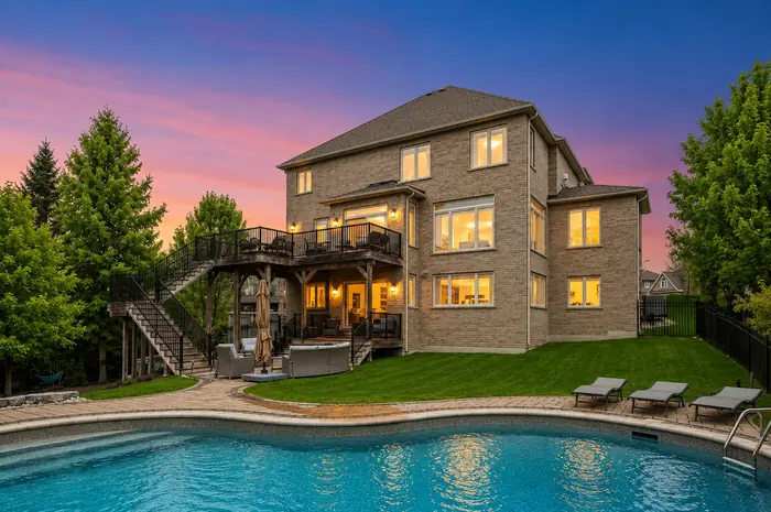 Rear of the home at dusk with lit windows, two-level deck and pool in the foreground, digitally enhanced image