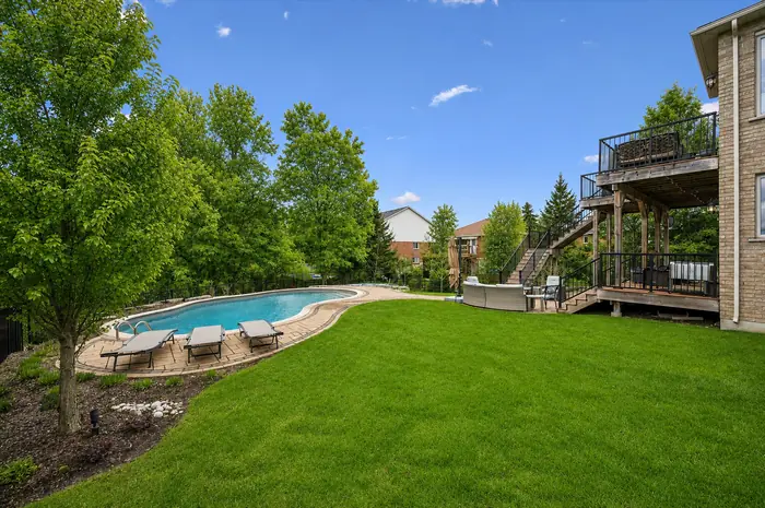Expansive level lawn with the pool and lounge deck along the treeline, digitally enhanced image